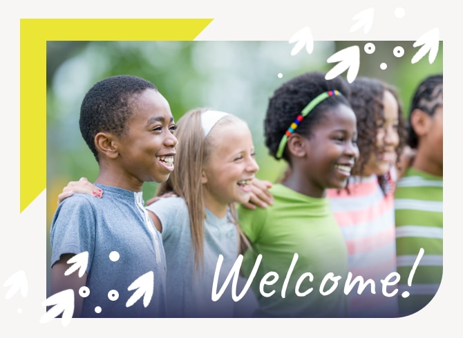 A line of young children stand outdoors, their arms on each others’ shoulders, smiling and looking off-camera to the right. They are a mix of ages, races, and hairstyles. They wear colorful summer clothes in a variety of colors: blue, green, and yellow. Blurry trees are in the background.