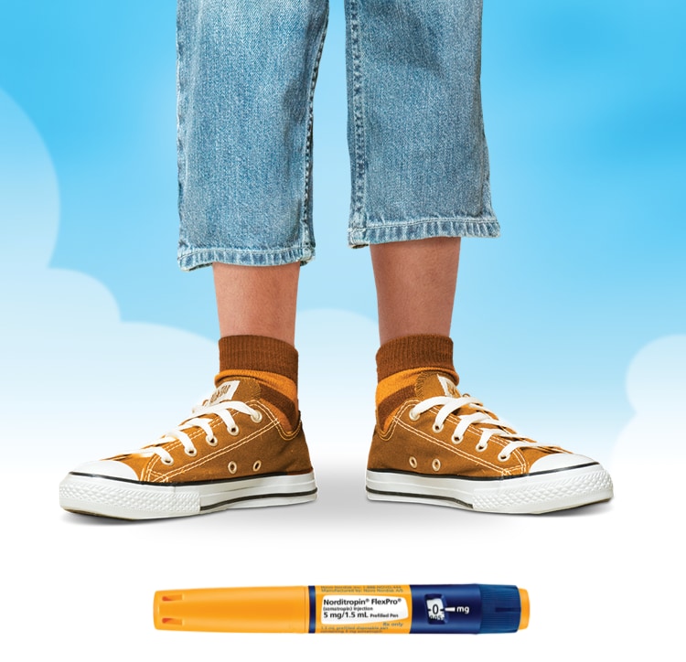 A young person pictured only from the knees down. They are wearing orange tennis shoes, colorful socks, and short jeans. A few inches of their calf is visible. Also pictured is a FlexPro® pen used for injections.