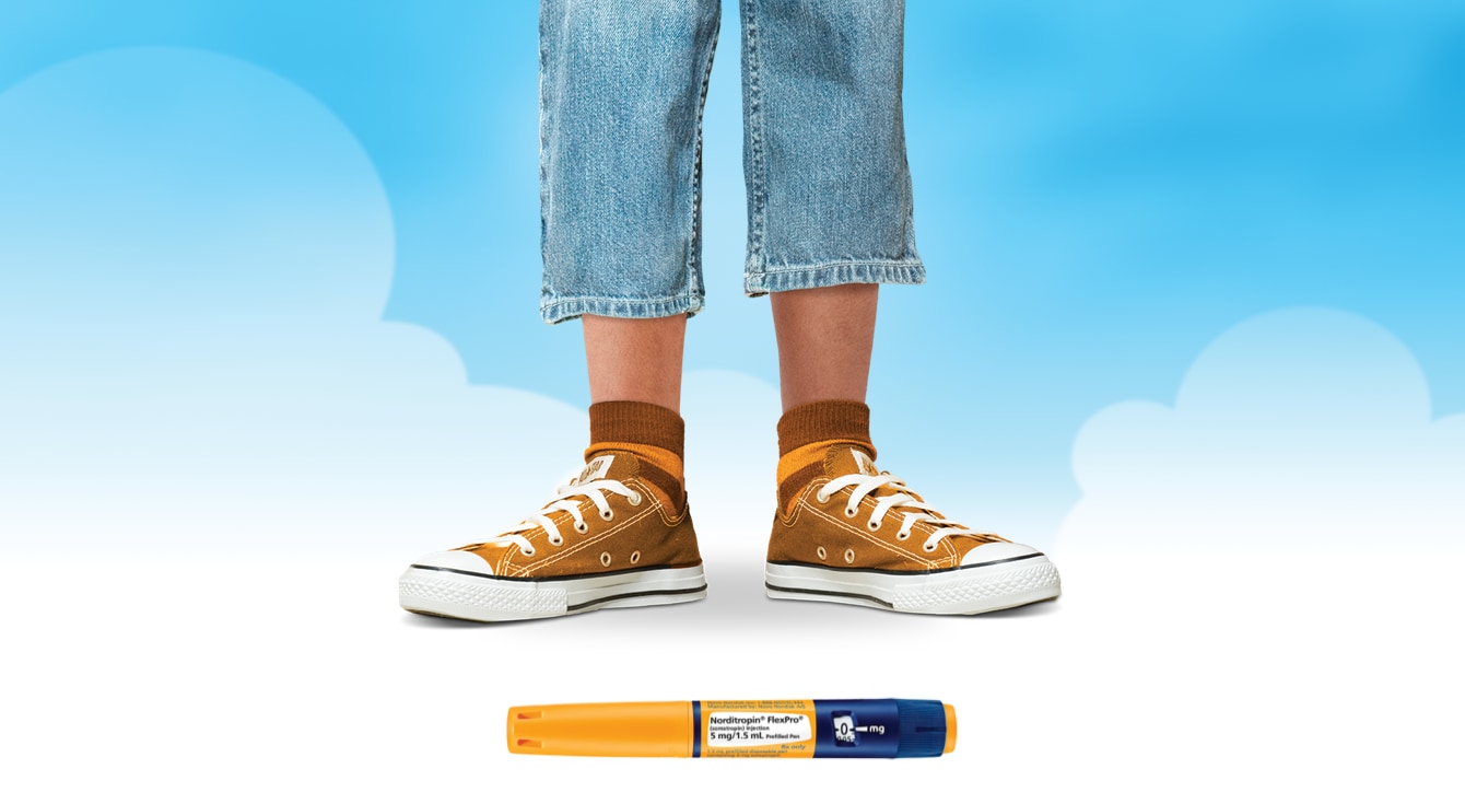 A young person pictured only from the knees down. They are wearing orange tennis shoes, colorful socks, and short jeans. A few inches of their calf is visible. Also pictured is a FlexPro® pen used for injections.